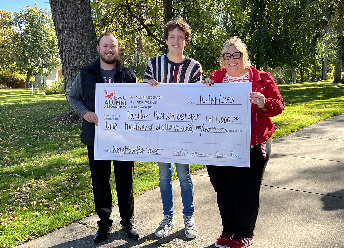 Scholarship winner pictured with big fake check and Alumni Association's Riley Baxter and Kelsey Hatch-Brecek.